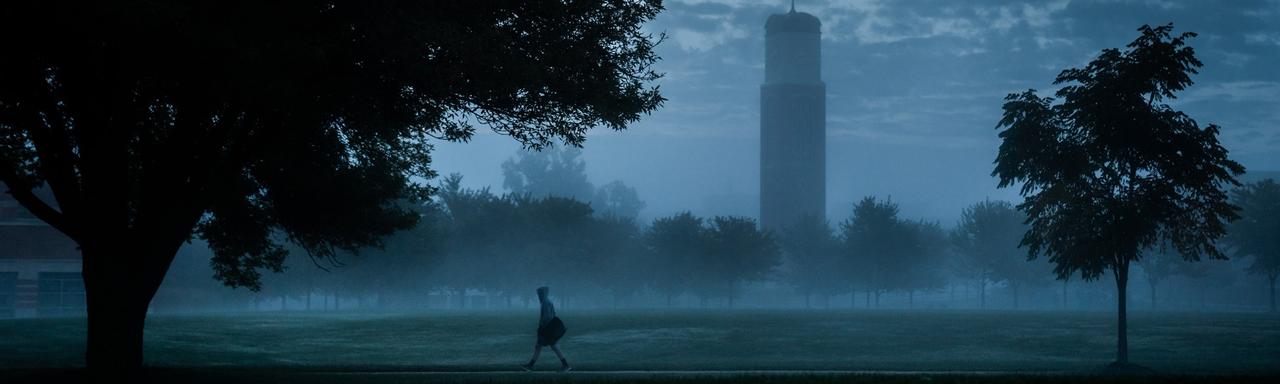 Foggy night on campus with student walking in front of Cook Carillon Clock Tower